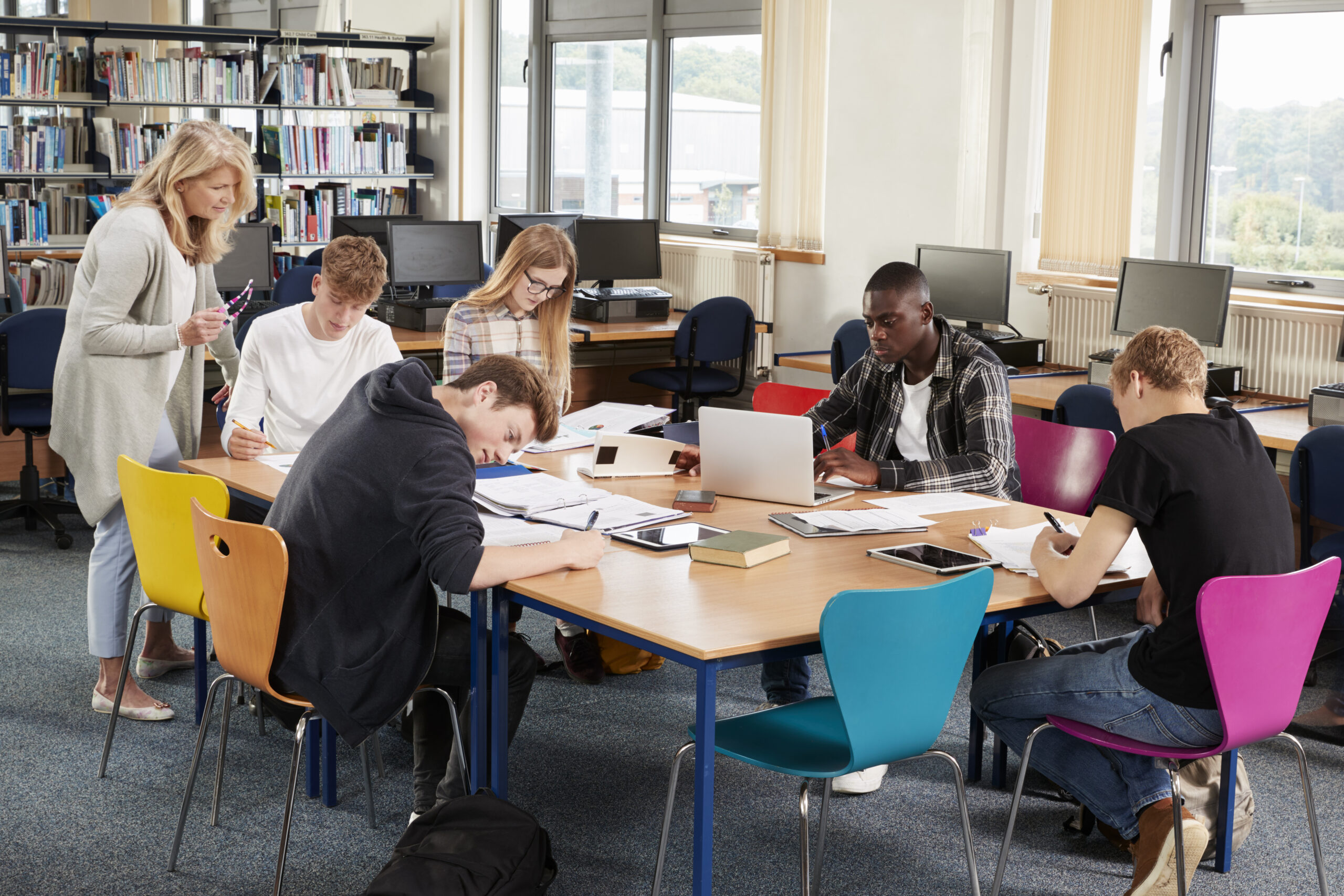 Busy College Library With Teacher Helping Students At Table